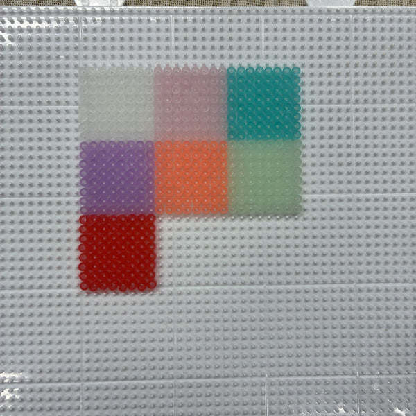 Gros plan sur les 7 coloris de perles à repasser phosphorescentes 2,6 mm sur plaque à picots