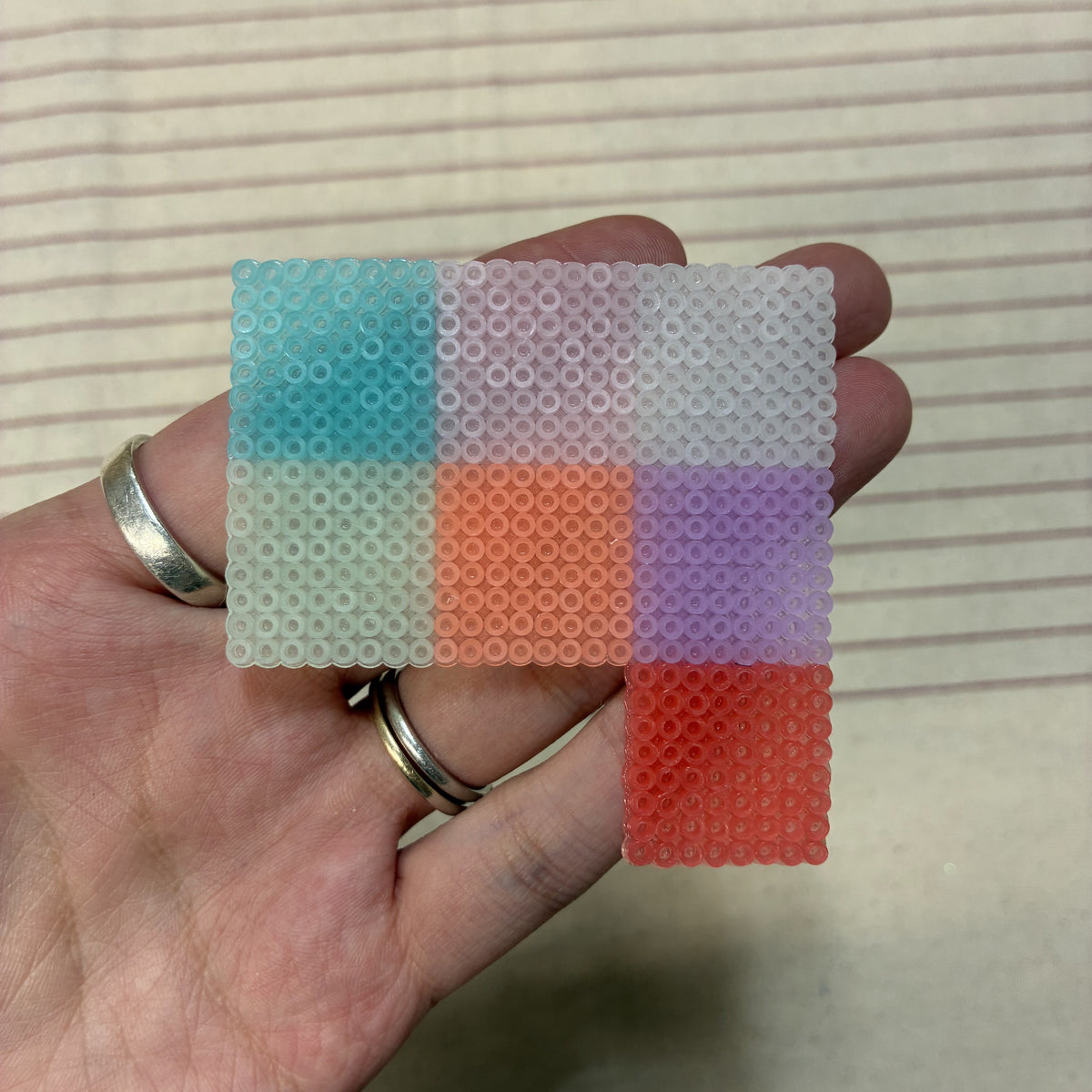 Nuancier repassé des 7 perles à repasser phosphorescentes 2,6 mm tenu en main, rendu translucide