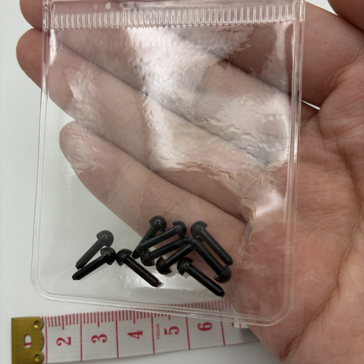 Sachet de 10 yeux noirs demi-boule à tige 3 mm tenu en main
